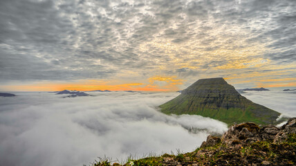 Panorama von Bergspitzen die aus den Wolken auf den Färör Inseln beim Sonnenuntergang ragen und...