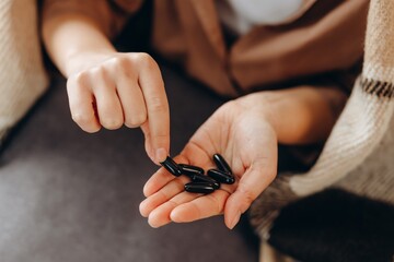 Dietary supplement, young woman, girl holding black medical pill, taking or eating vitamin C, D for skin, hair and nail treatment, strengthening glass of clean water at home, health care.