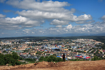 A man stands on a mountain cliff, against the backdrop of Petropavlovsk-Kamchatsky, on a clear sunny day, clouds, a volcano.