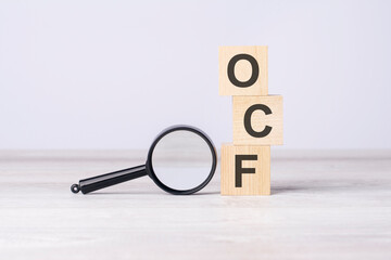 concept Operating Cash Flow or OCF. text on wooden cubes under a magnifying glass.