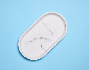 Empty white oval marble plate on a blue background, top view