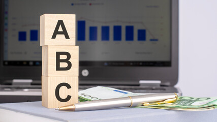 close-up of wooden blocks with the word ABC and banknotes on the background of a laptop