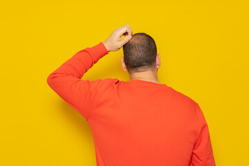 Back view of thoughtful man scratching his head over yellow background. He is doubting his...