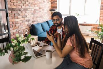 Young millennial indian husband and wife doing domestic paperwork, accounting job and reviewing...