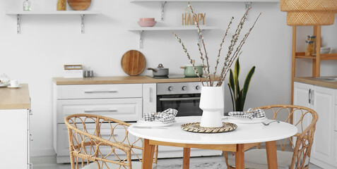 Vase with willow branches on dining table in interior of light kitchen