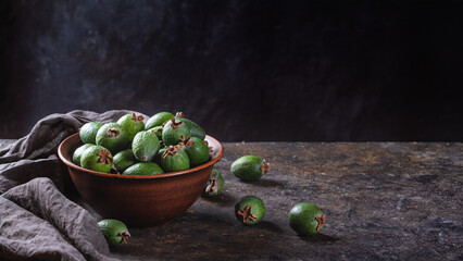 Tropical fruits green ripe feijoa sellowiana berries in a clay bowl and on a table on a dark background. Kitchen background banner with space for text.
