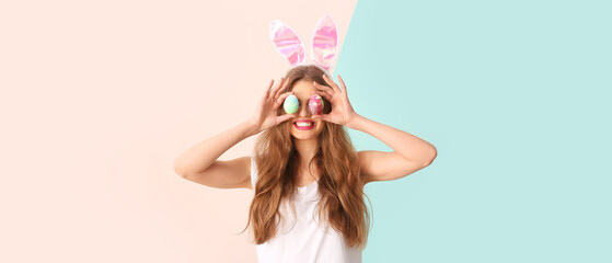 Funny young woman with Easter bunny ears and painted eggs on color background