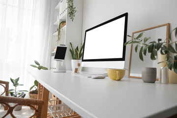 Modern workplace with computer and tablet near light wall