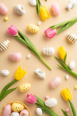 Easter concept. Top view vertical photo of colorful easter eggs in bowl ceramic easter bunnies yellow and pink tulips on isolated light beige background