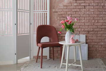 Vase with tulips and Easter bunny on end table and armchair near brick wall