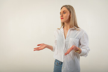 Portrait of a young, emotional, happy girl without makeup, smiling at the camera, gesturing with her hands, standing on a white background. Place for writing
