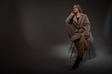 portrait of a young, emotional girl sitting on a chair in a flirtatious mood, gesturing with her hands, empty space, wearing a jacket, a dark cloak on an isolated white background, space for text