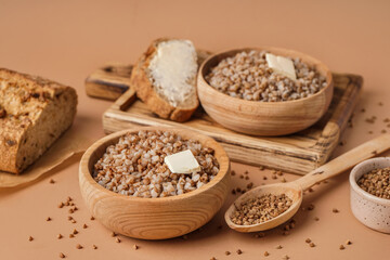 Wooden bowls of tasty buckwheat porridge with butter and bread on beige background