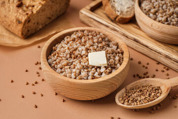 Wooden bowl of tasty buckwheat porridge with butter on beige background