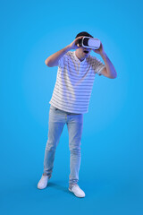 Young man using VR glasses on light blue background