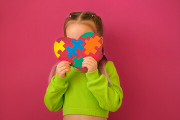 A shy child with autism syndrome hides behind a heart decorated with colorful puzzles. Equality and support in society