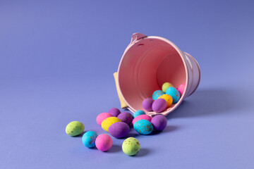 Image of multi coloured easter eggs and bucket with copy space on purple background