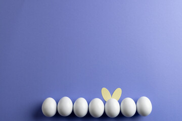 Image of row of white easter eggs with bunny ears and copy space on purple background