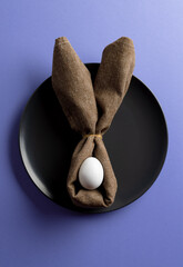 Image of white easter egg and bunny ears on black plate and copy space on purple background