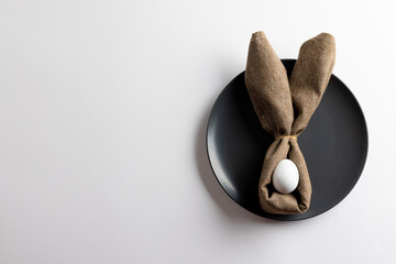 Naklejka premium Image of white easter egg and bunny ears on black plate and copy space on white background