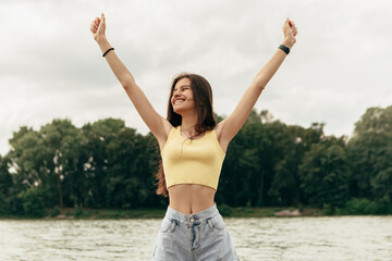 Slim happy smiling woman stand in river sea lake. Female on beach island, splashing waves foam. Girl tourist on vacation wide open hands spreading, weekend relaxing resting resort. Lady sunbathing

