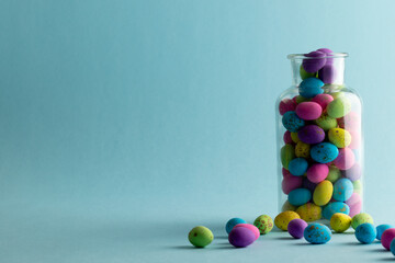Fototapeta premium Image of multi coloured easter eggs in clear jar with copy space on blue background