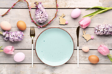 Table setting with Easter eggs, cutlery and flowers on grey wooden background