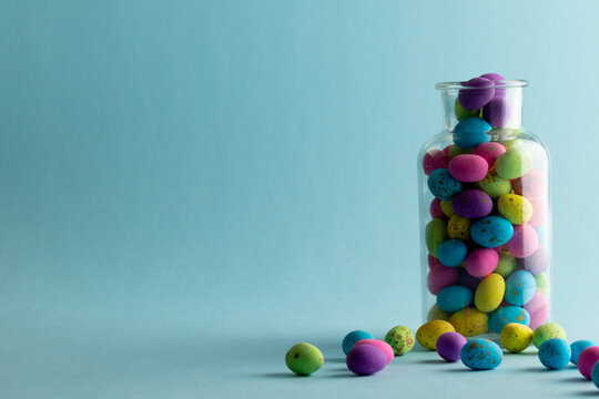 Image of multi coloured easter eggs in clear jar with copy space on blue background