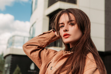 Caucasian young pretty stylish woman day walking street dressed brown trench coat smiling happy poses outside in city, spring autumn season. Cute brunette hair lady in good mood
