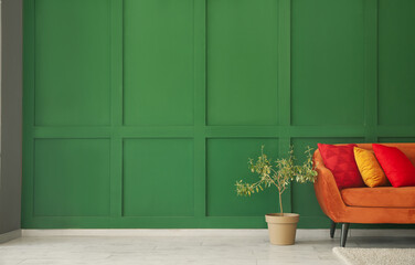 Red sofa with stylish cushions and houseplant near green wall