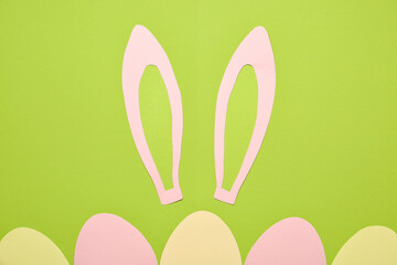 Paper bunny ears and Easter eggs on green background