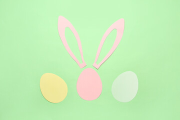 Paper bunny ears and Easter eggs on green background