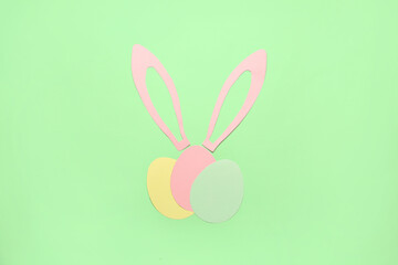 Paper bunny ears and Easter eggs on green background