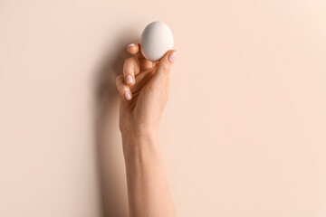 Woman holding egg on beige background