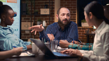 Business meeting, man explaining marketing strategy plan, coworkers discussing company report presentation. Employees communication in boardroom, diverse office workers teamwork