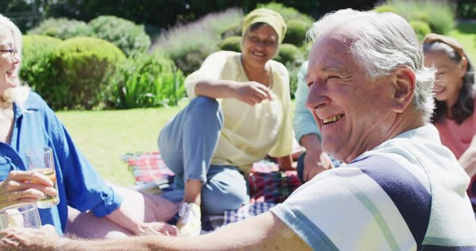 Happy senior caucasian man laughing at a picnic with diverse friends in sunny garden, slow motion