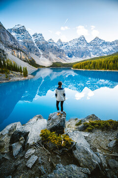 Adventurous woman on the edge of a cliff overlooking the beautiful Canadian Rockies and Moraine Lake during autumn. Banff National Park, Alberta, Canada.