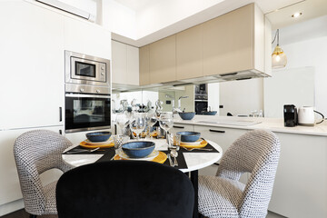 Round white marble dining table surrounded by upholstered chairs in a corner of an open plan loft kitchen
