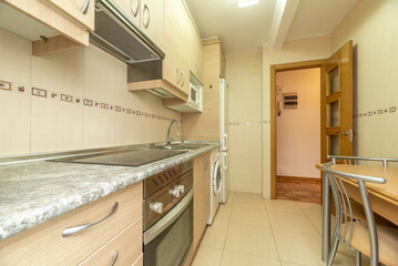 Kitchen with birch wood furniture with metal handles, integrated electromessives of various colors, wooden table and matching chairs and light tiles