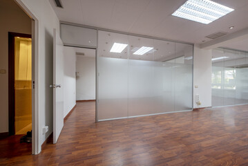 Offices of an empty office with technical ceilings, glass partitions and reddish floating flooring