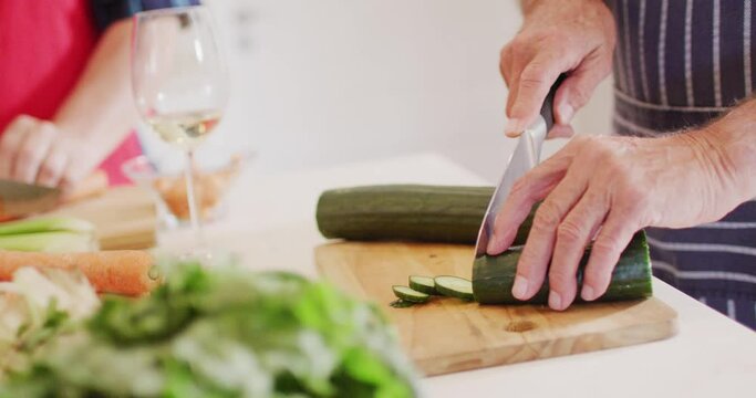 Senior caucasian man chopping courgette, preparing food in kitchen with friends, slow motion