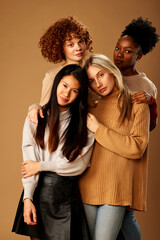 Multicultural girls with pure natural skin posing in studio and looking at the camera isolated on brown background.