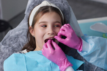 Cut view hands in latex gloves to floss child front teeth. Woman hold dental tools beside.