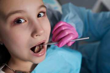 A close-up of a young girl getting a dental exam by dentist and using dental mirror to see baby...