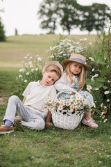 Cute little girl in daisy wreath is walking with her elder brother on the camomile field on the sunset.