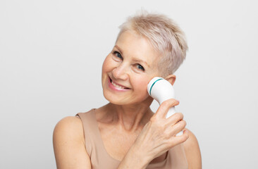 Naklejka premium Beautiful 60s woman holding a massager in her hand and use on face. Spa technique skincare ads.