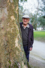 senior man hidden behind a tree trunk looking at camera. Old age lifestyle