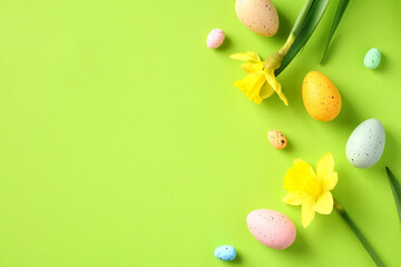 Flat lay composition with colorful Easter eggs and daffodil spring flowers on green background. Happy Easter greeting card design. Top view, copy space.