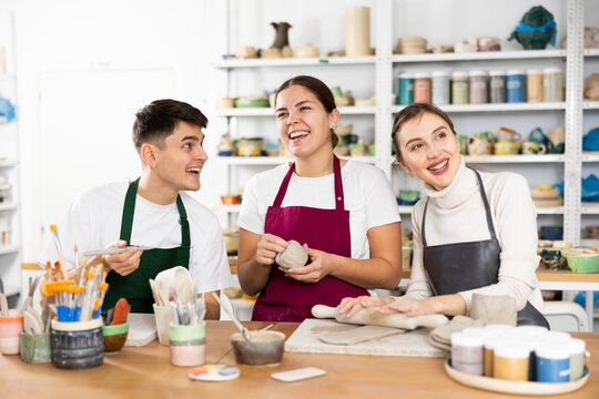 Two young women and young man making clay pottery in workshop