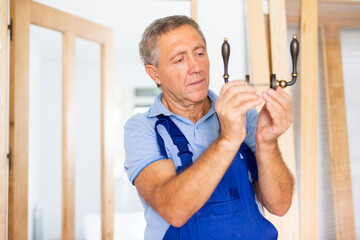 Fototapeta premium Serious middle-aged male locksmith examining a doorknob before installing it on a door in a house